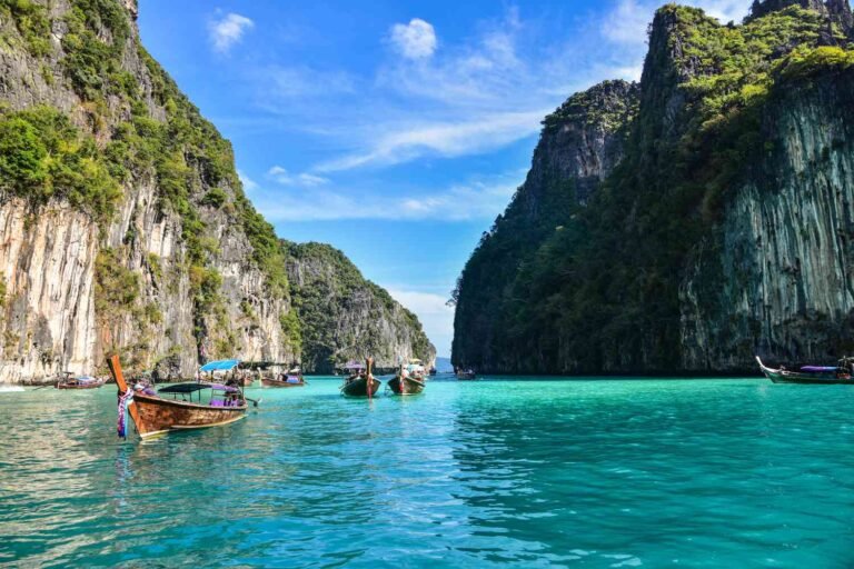 Longtail boats on turquoise water between limestone cliffs in Thailand’s Phi Phi Islands.